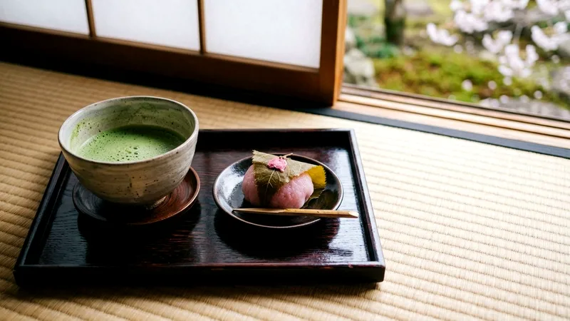 Pink sakura mochi sweets and matcha tea on a lacquered tray.